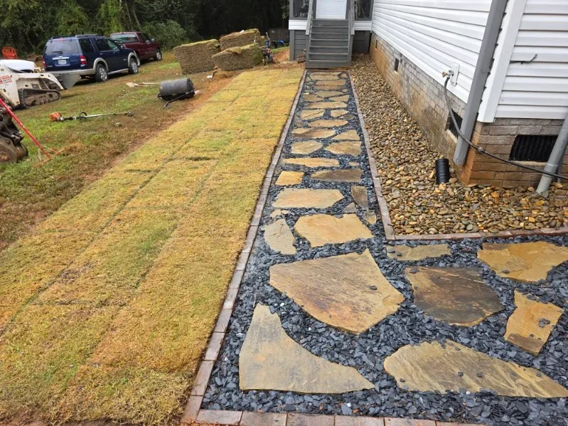 Flagstone pathway with black rock bed and metal edging along house foundation