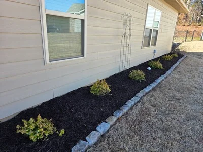 Black mulch foundation planting bed with shrubs and concrete edging along home exterior