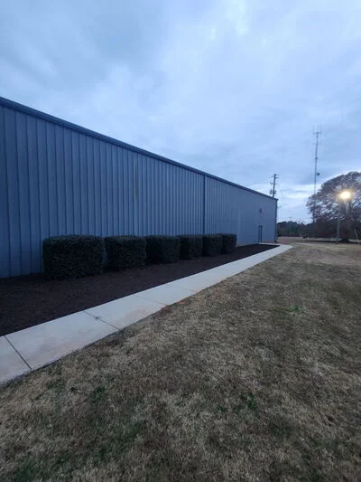 Metal building with black mulch beds, evergreen plantings, and concrete walkway